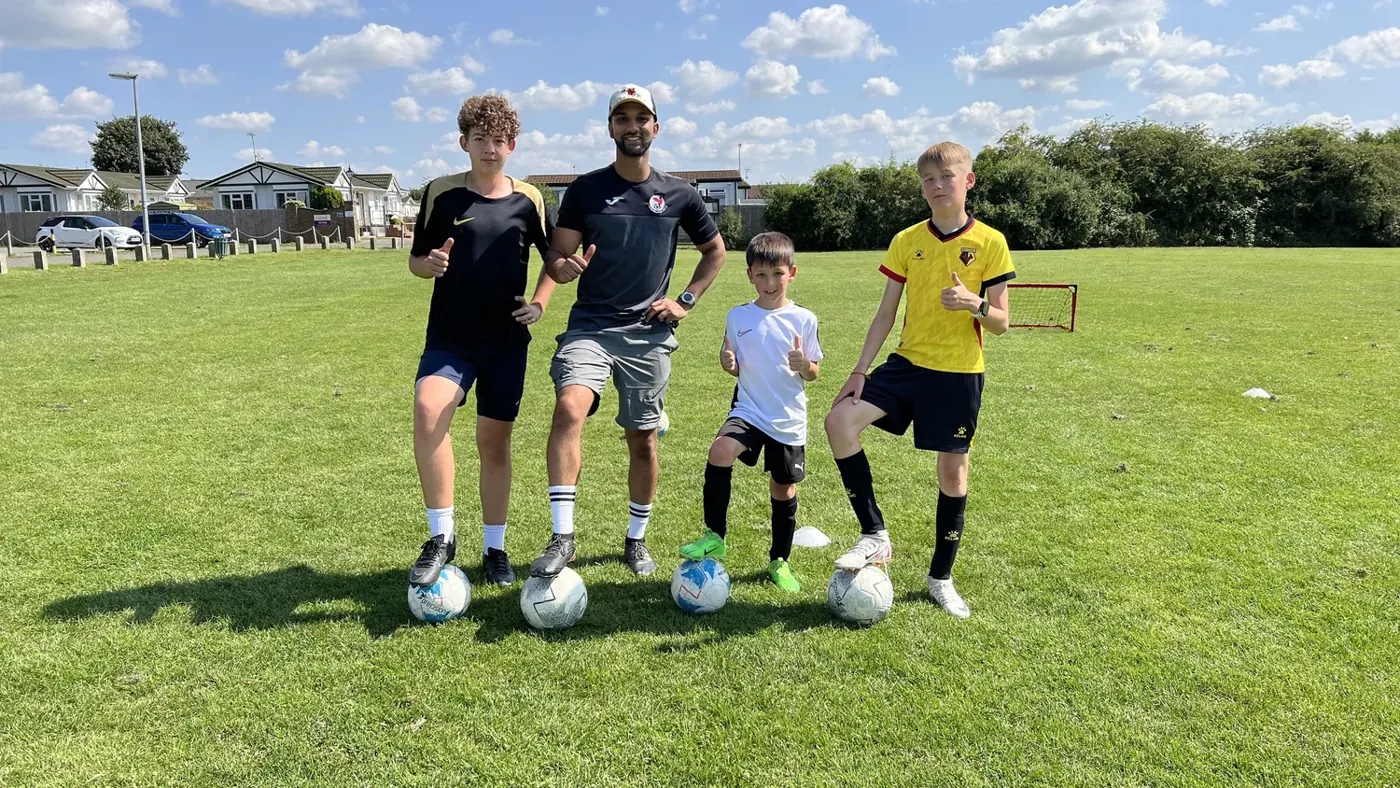 Coach Farhan with four young players and their footballs on a grass pitch